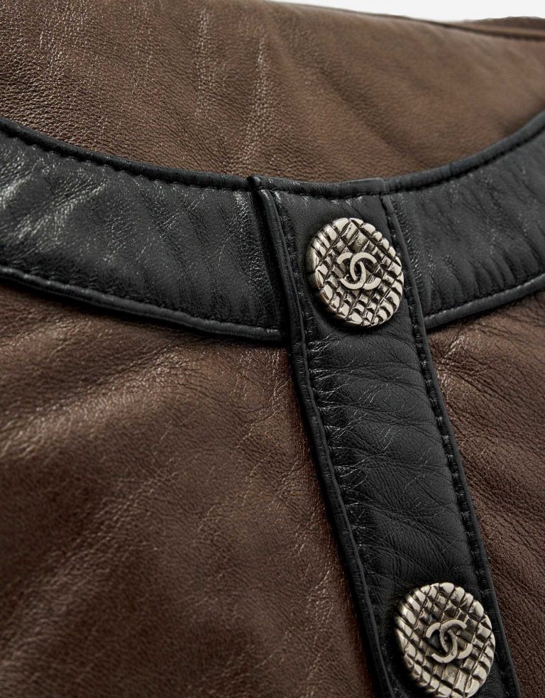 Button detail with Chanel logo of a pre-loved Chanel Girl Medium Lambskin in Brown and Black on SACLÀB